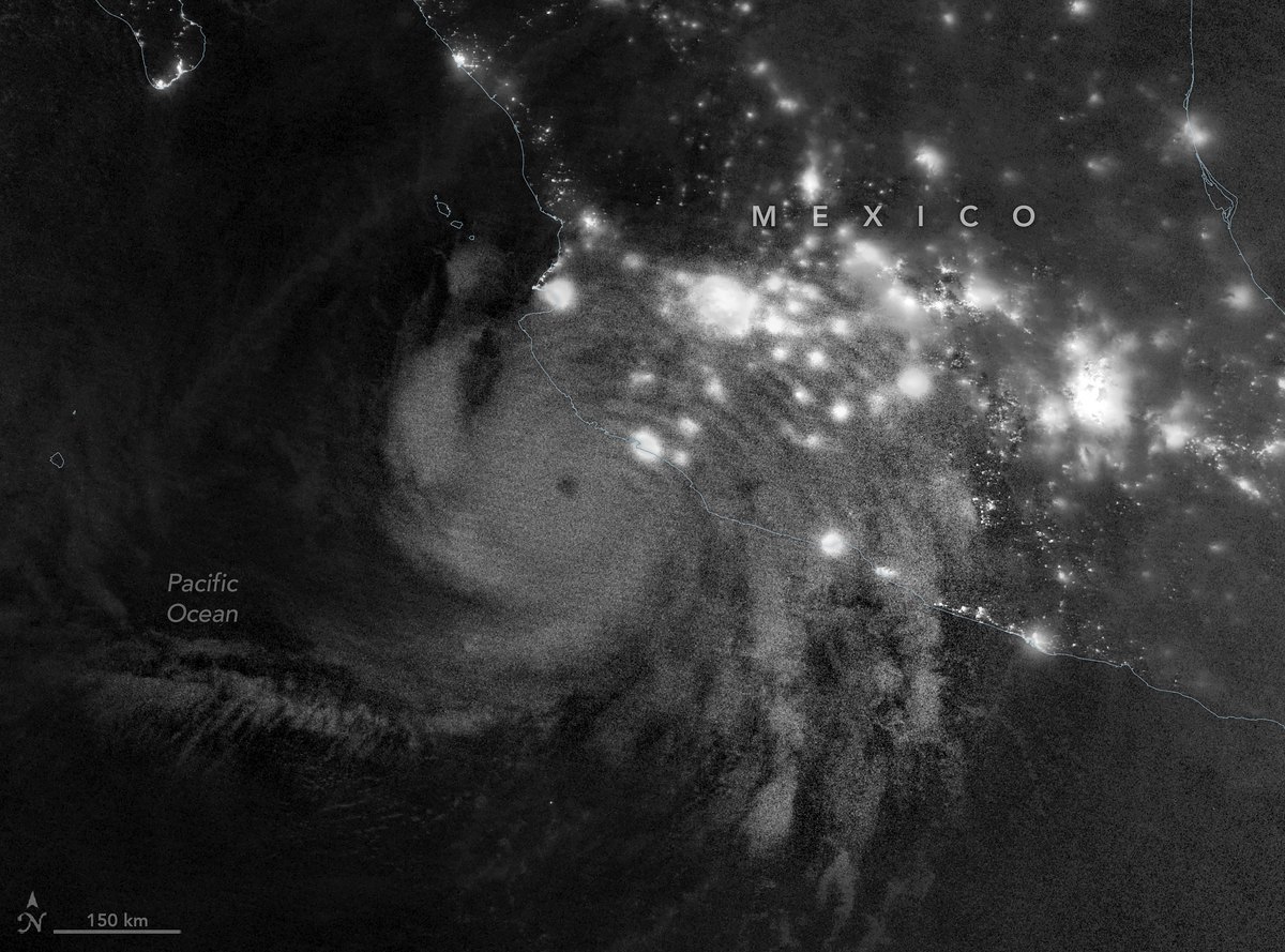 A grayscale night-time satellite image showing a semicircle of fine ripples spreading across the sky, with hurricane clouds and the city lights of Mexico below.