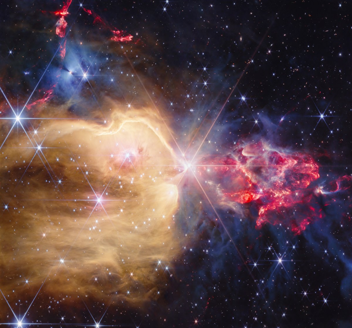 A glowing stellar nursery with golden gas, grey clouds, red jets and bright stars against dark space.