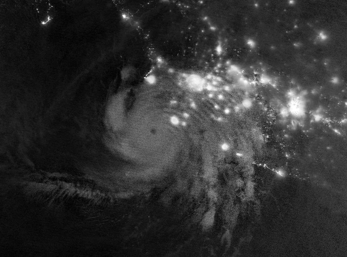 Black-and-white satellite image showing curved bands of light above the cloud structure of Hurricane Simon.