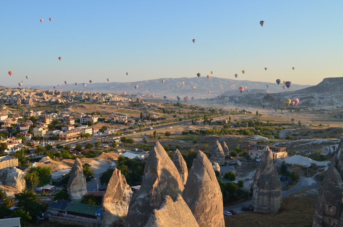 Colourful balloons floating over sunlit pale stone formations and valleys.