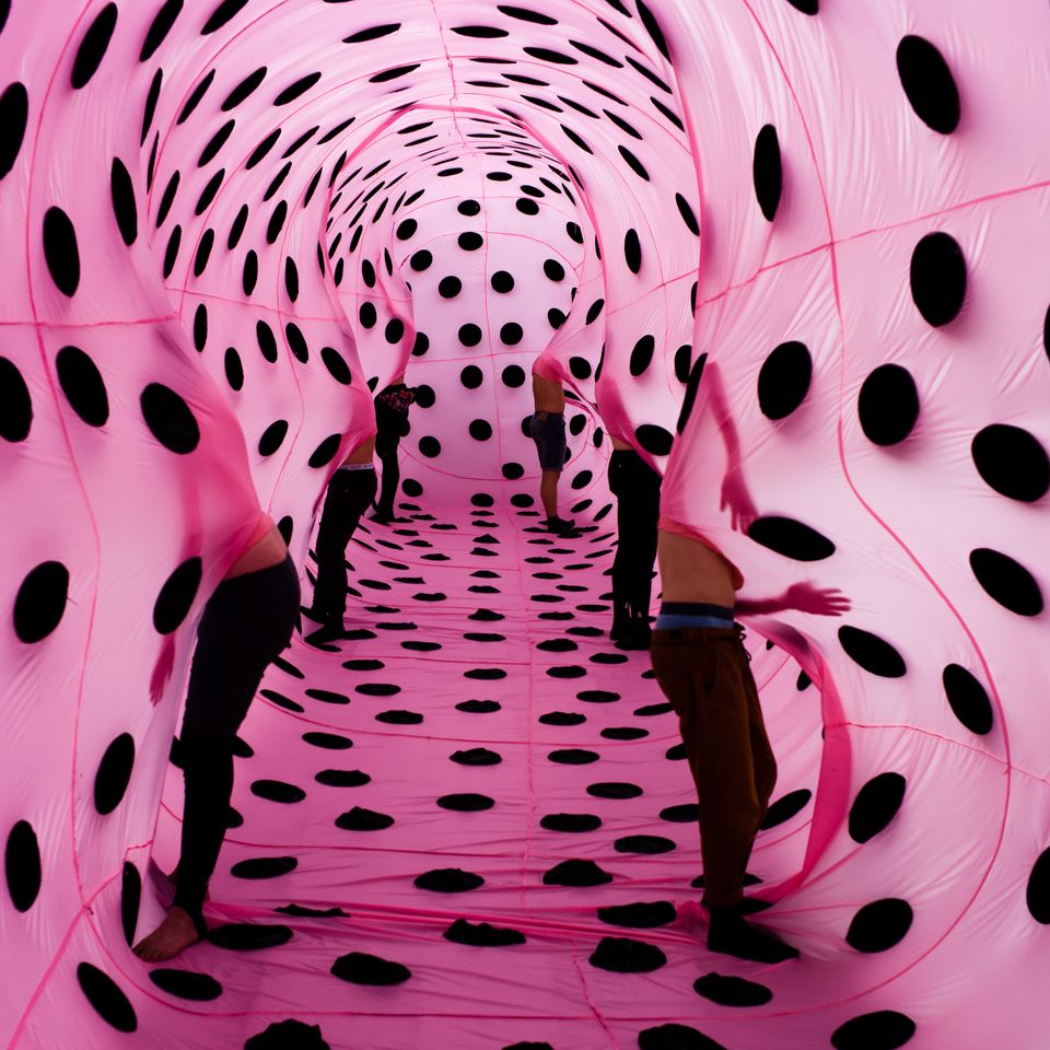 Visitors standing inside a bright pink inflatable tunnel covered with large black polka dots.