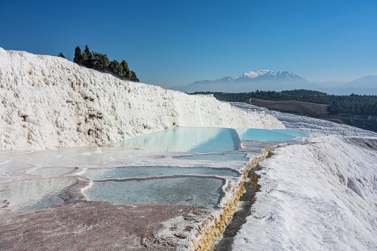 White cascading limestone terraces filled with pale blue water on a hillside.