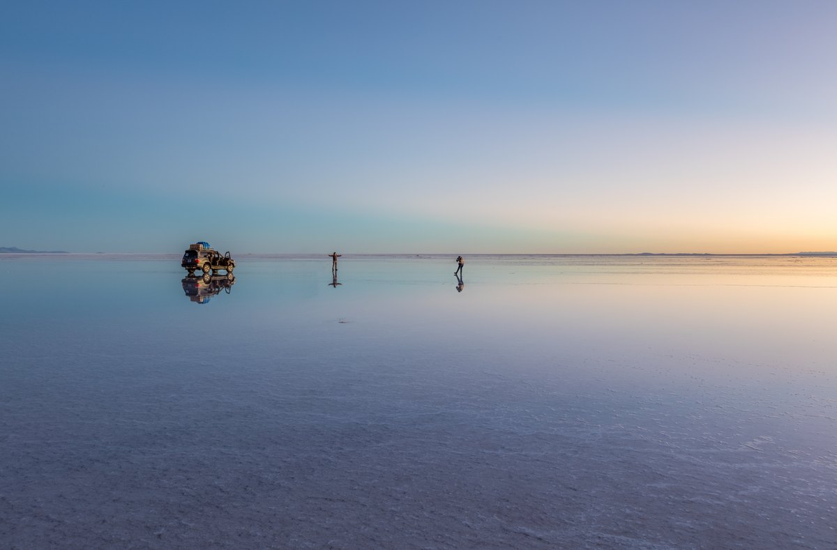 Sunrise over shallow reflective water on the salt flat, with clouds mirrored across the horizon.
