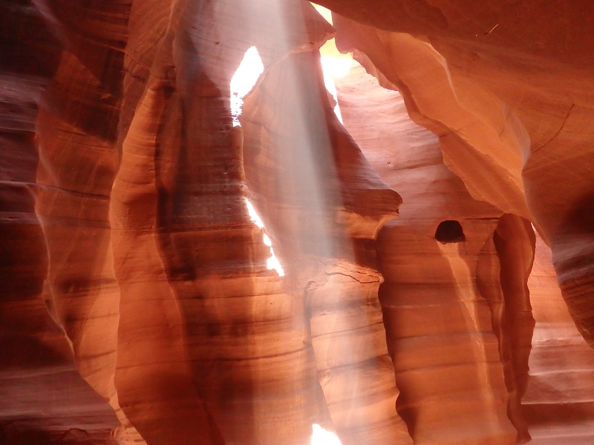 Golden shafts of sunlight descending between flowing orange sandstone walls.