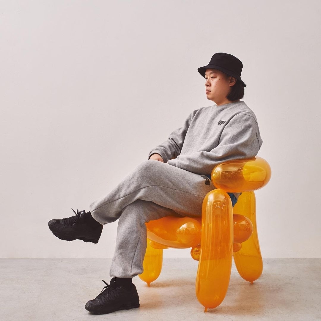 A person in grey clothing sitting on a bright translucent orange chair assembled from large balloon-shaped forms.