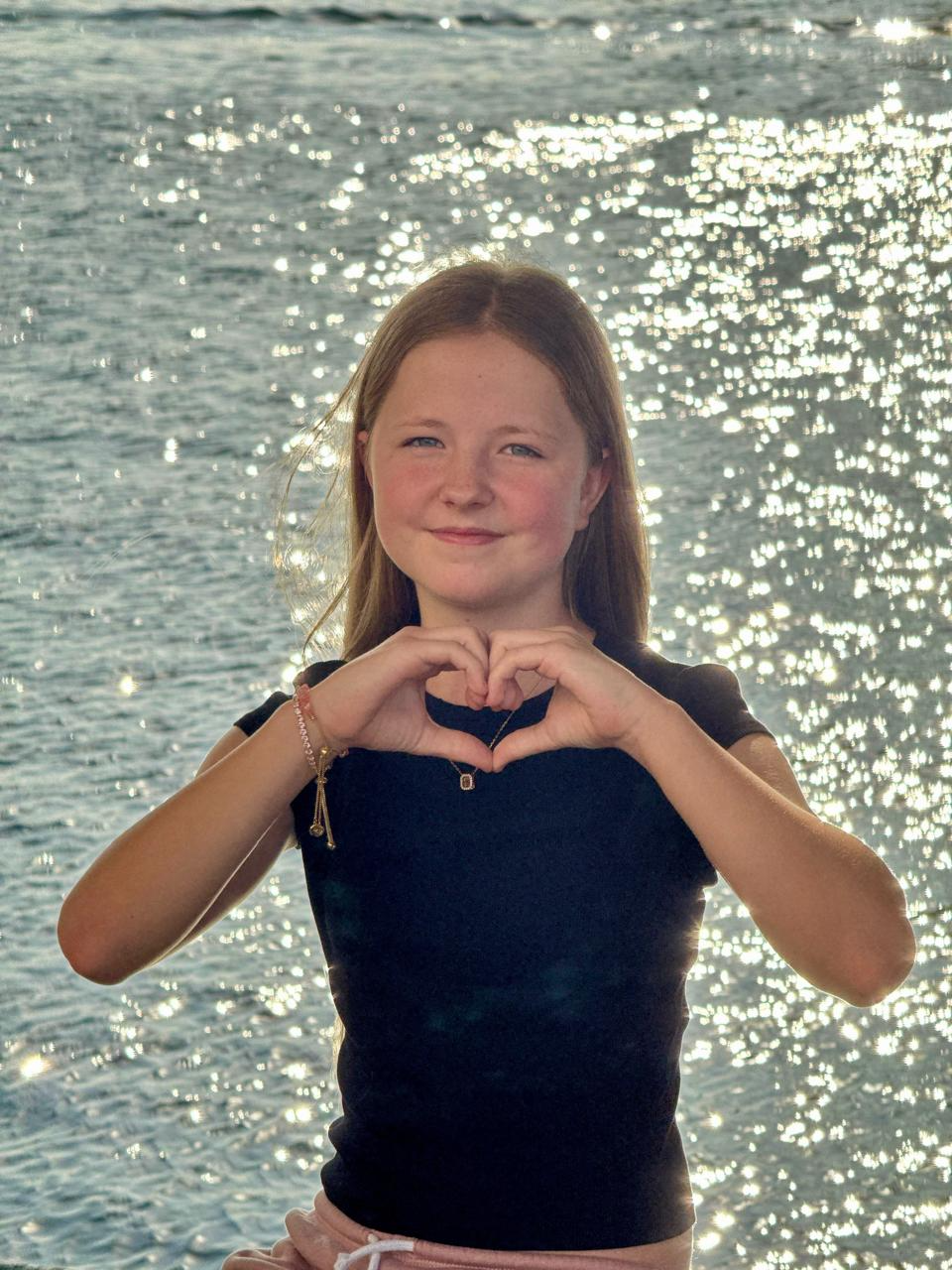 Aimee, founder of BEST OF, making a heart shape with her hands by the sea