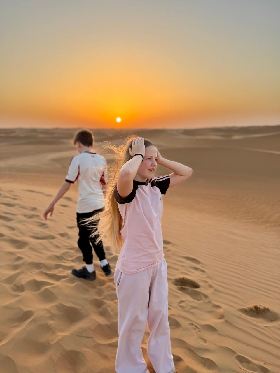 Aimee in the desert at sunset with her brother walking behind