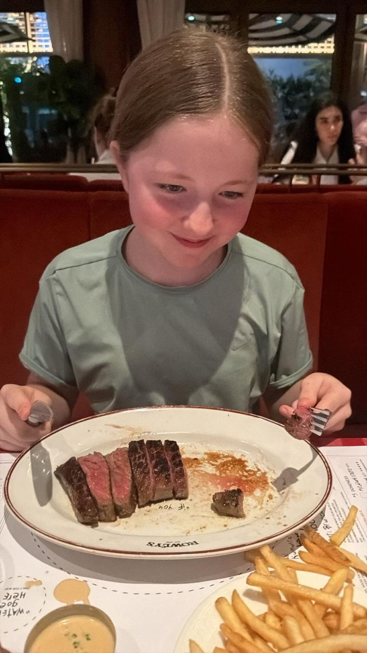 Aimee smiling at a plate of sliced steak and fries in a restaurant
