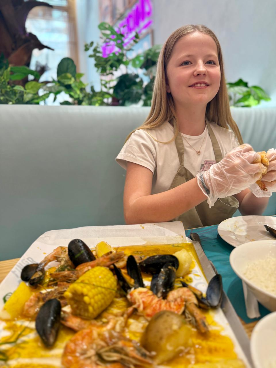 Aimee smiling behind a tray of prawns, mussels and corn, wearing plastic gloves