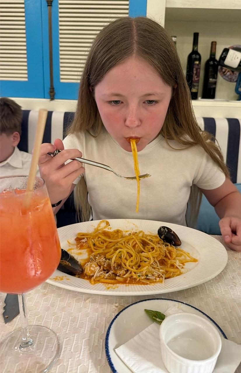 Aimee slurping a strand of spaghetti vongole, with clams on the plate