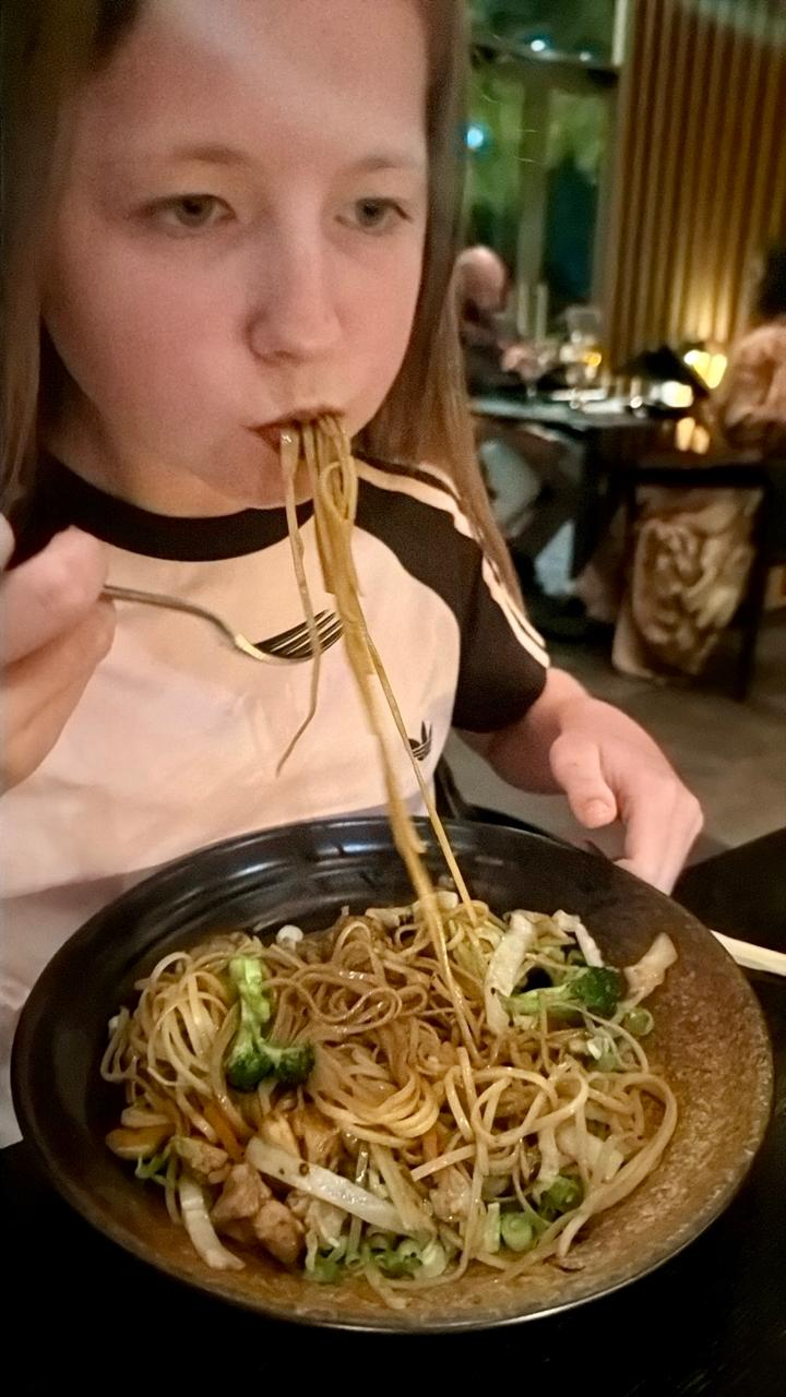 Aimee eating a bowl of noodles with a fork