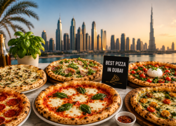 A selection of wood-fired pizzas with fresh toppings on a table overlooking the Dubai skyline and Burj Khalifa at sunset.