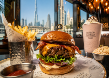 Gourmet cheeseburger with crispy fries and a milkshake at an upscale Dubai restaurant with city skyline views.
