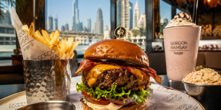 Gourmet cheeseburger with crispy fries and a milkshake at an upscale Dubai restaurant with city skyline views.