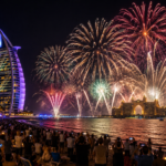 Fireworks lighting the Dubai coastline at night, with Burj Al Arab, Atlantis The Palm and spectators by the water.