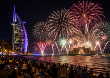 Fireworks lighting the Dubai coastline at night, with Burj Al Arab, Atlantis The Palm and spectators by the water.