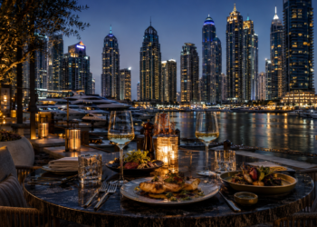 Elegant waterfront restaurant dining in Dubai Marina at night, with marina yachts, candlelit tables and illuminated skyscrapers in the background.
