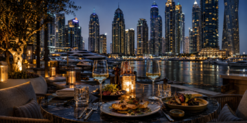 Elegant waterfront restaurant dining in Dubai Marina at night, with marina yachts, candlelit tables and illuminated skyscrapers in the background.