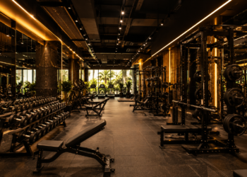 A premium Dubai gym interior with strength equipment, dumbbells, squat racks, cardio machines and warm modern lighting.